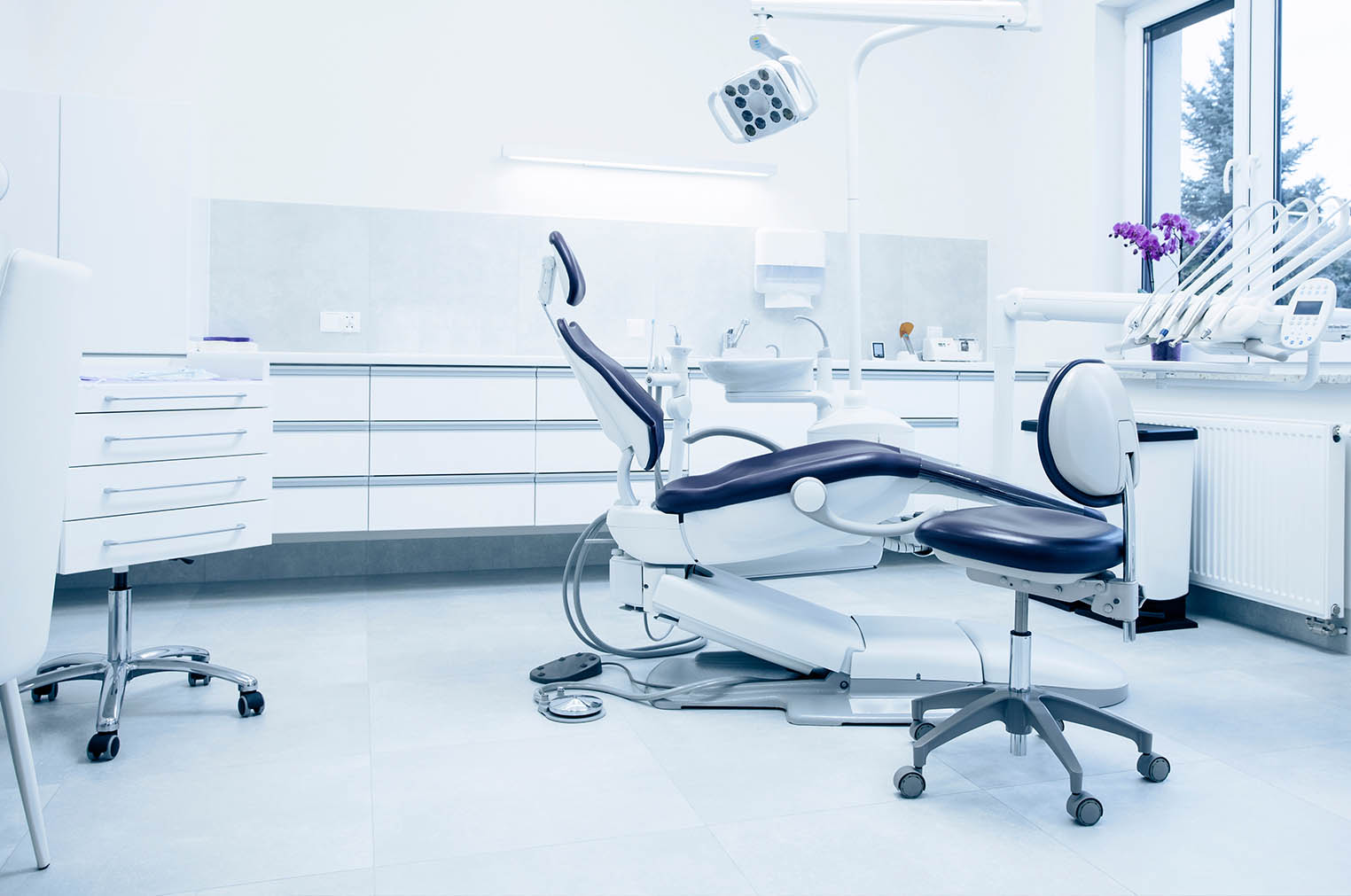 The image shows a modern dental clinic interior with various pieces of equipment, including a dental chair and an X-ray machine.