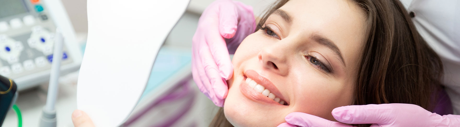 A person is seated in a dental chair, receiving care from a dental professional who stands behind them.